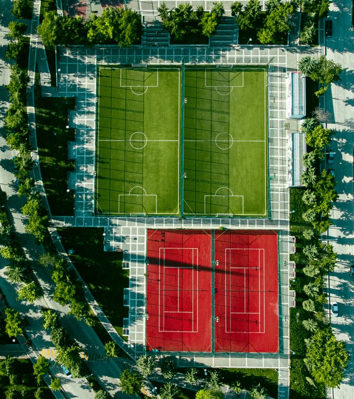 Top view of soccer and tennis courts framed by greenery in an urban park setting.